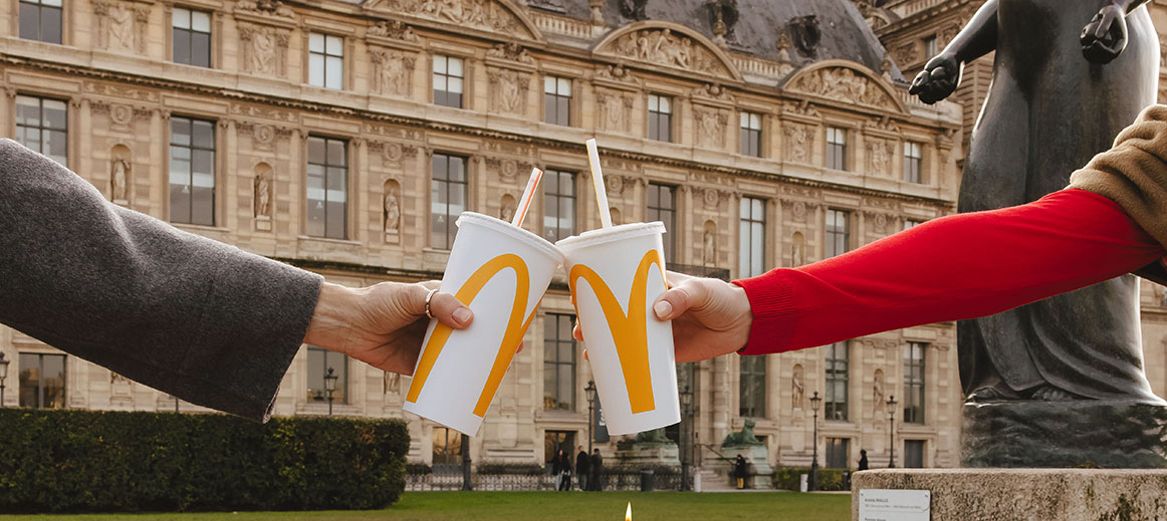 McDonald's Europe. two hands holding a McDonald's beverage cup in front of a building