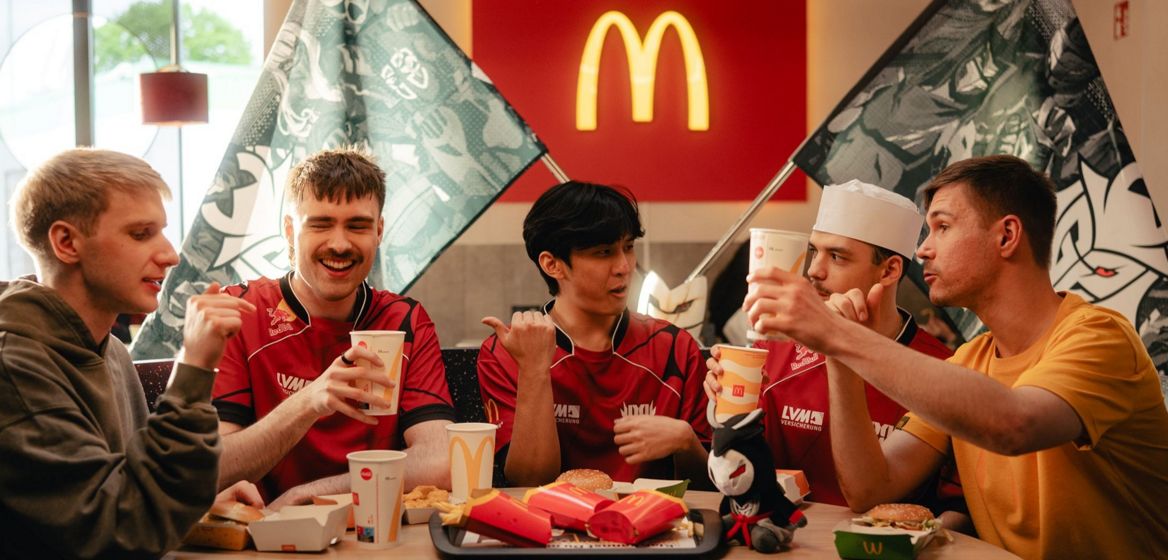 Eine Gruppe junger männlicher Personen speisen an einem Tisch in einem McDonald’s Restaurant und haben gute Laune.