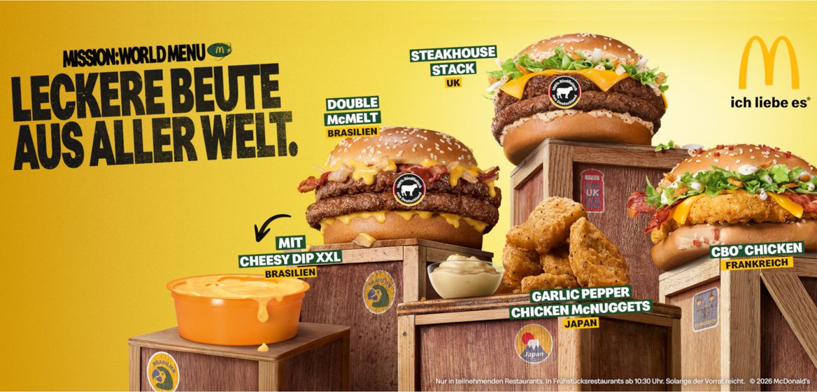Werbebanner von McDonald's zur Aktion „Mission: World Menu“. Vor gelbem Hintergrund sind fünf Aktionsprodukte auf Holzkisten zu sehen: „Double McMelt (Brasilien)“, „Steakhouse Stack (UK)“, „CBO Chicken (Frankreich)“, „Garlic Pepper Chicken McNuggets (Japan)“ und „Cheesy Dip XXL (Brasilien)“. Links steht der Slogan „MISSION: WORLD MENU – LECKERE BEUTE AUS ALLER WELT.“, rechts das McDonald's-Logo mit dem Schriftzug „ich liebe es®“.