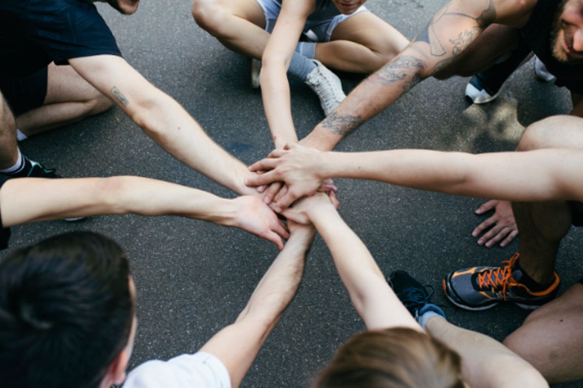 A group of amateur athletes bring their hands together in a show of unity and sportsmanship before playing a friendly game of basketball outdoors.