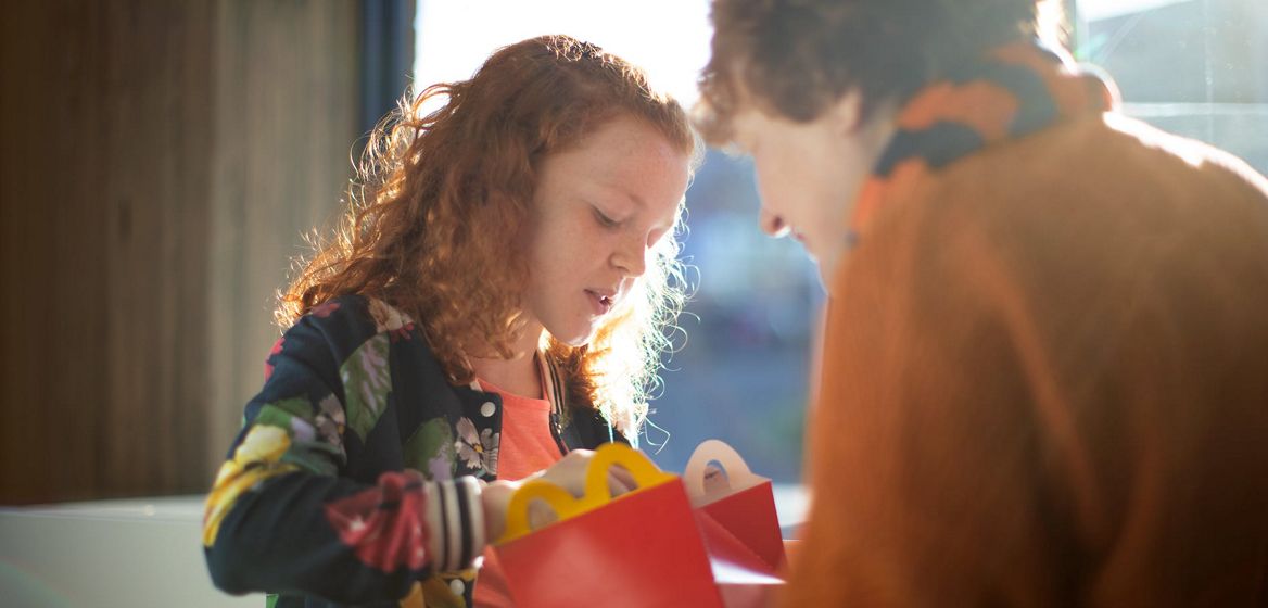 A girl eating a happy meal with an adult in the foreground