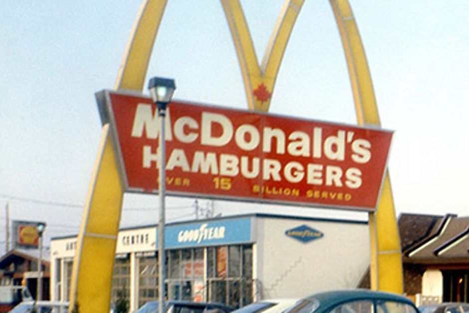 Un affichage rétro de McDonald’s montrant les arches devant un restaurant