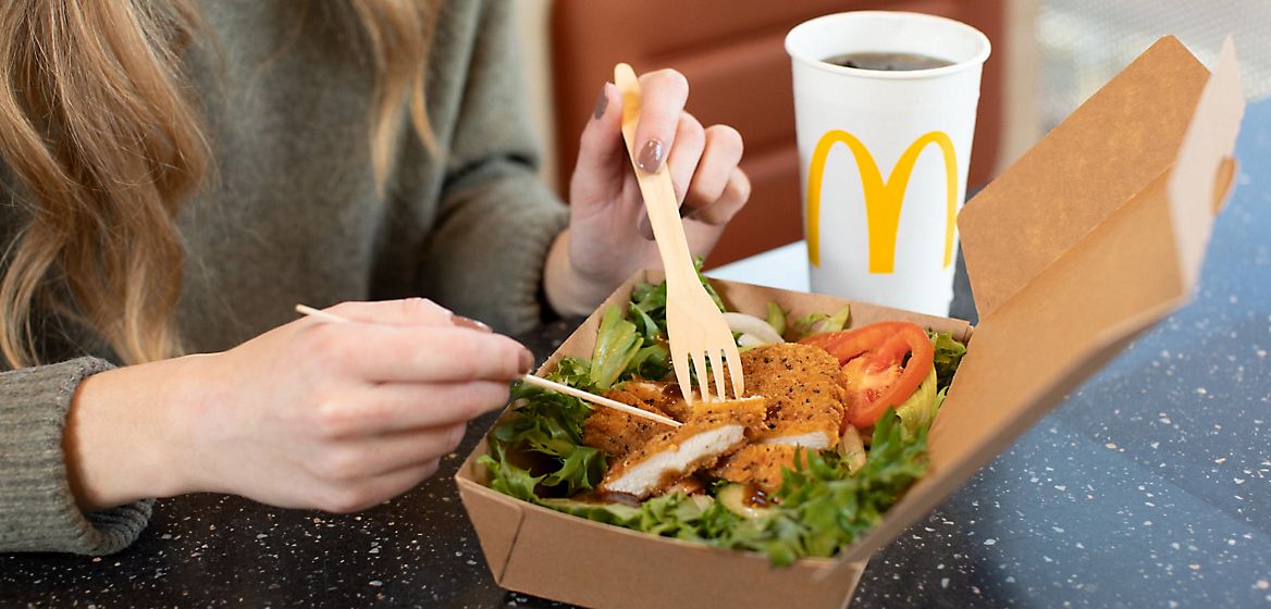 Close-up of a woman's hands while eating a McDonald's salad with a drink in the background