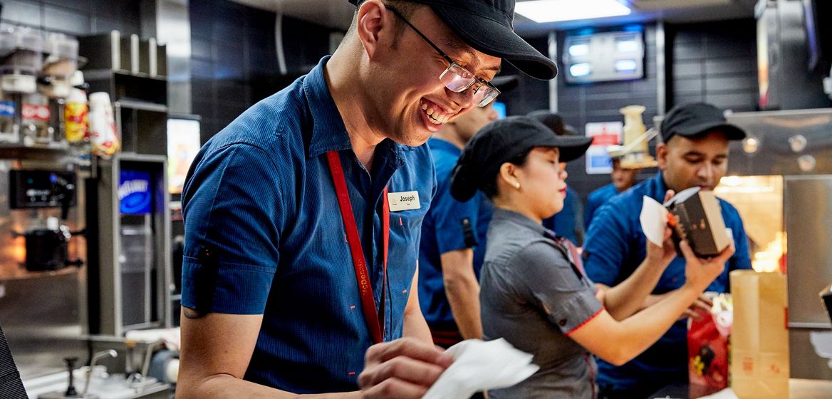 A McDonald's employee smiling in the foreground with other employees working in the background