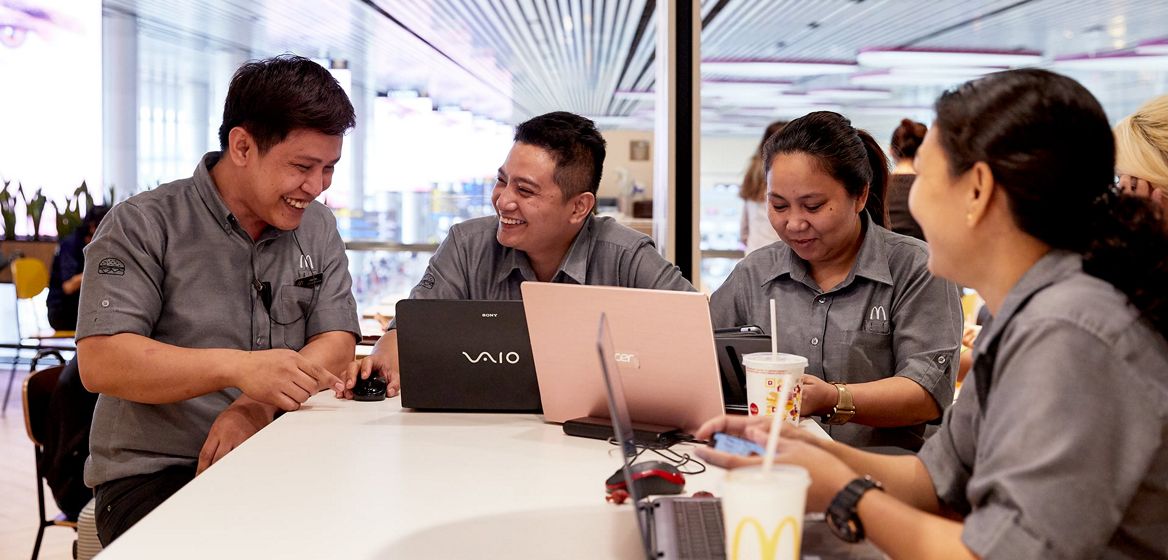 McDonald's employees smiling around a table with laptop computers