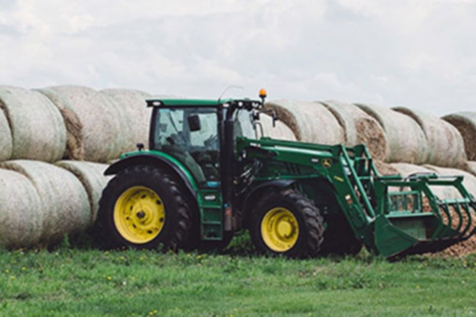 A green tractor in front of multiple hay bales on a bright sunny day