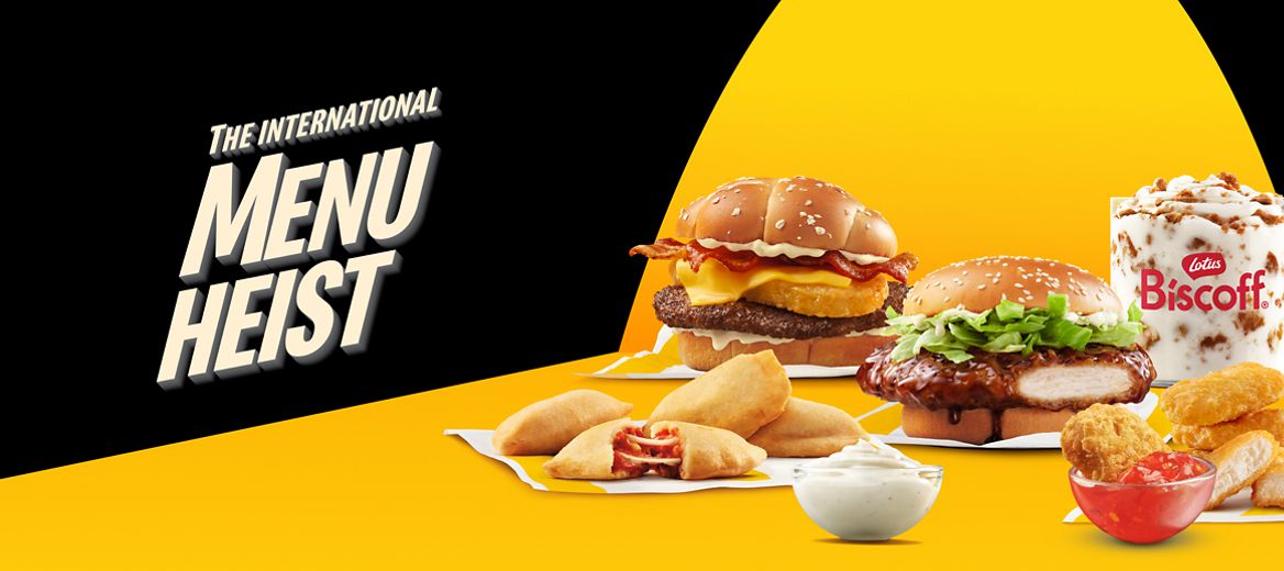 A spotlight illuminating a series of international McDonald’s menu items including a Big Rösti Burger, a Chicken Teriyaki Sandwich, a Biscoff® McFlurry®, McPizza Bites, McNuggets, a Garlic Mayo-Style Sauce, and a Sweet Tangy Chili Dip. Next to them are the words “The International Menu Heist”.