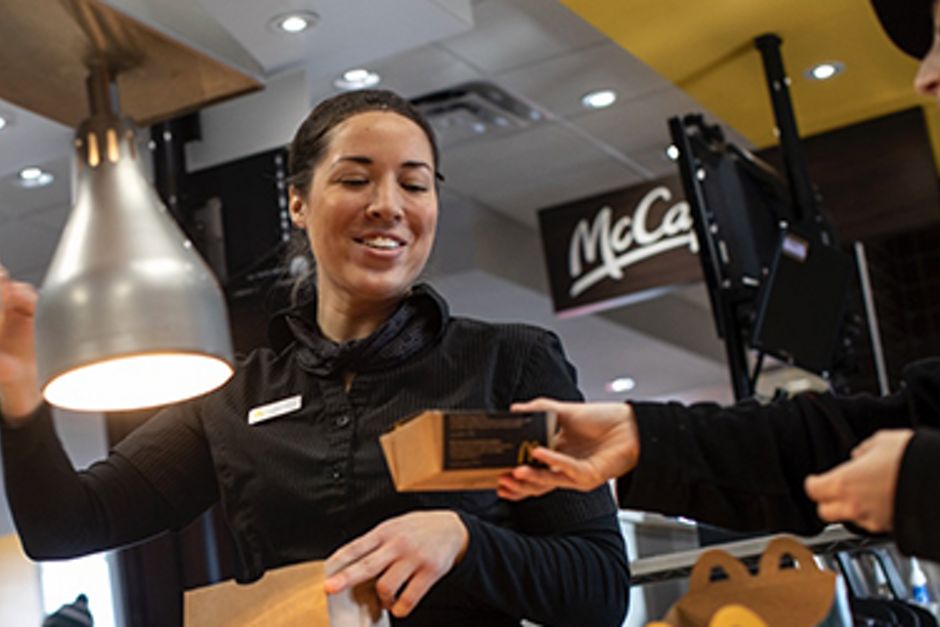 McDonald's staff member cheerily packing an order into a brown food bag