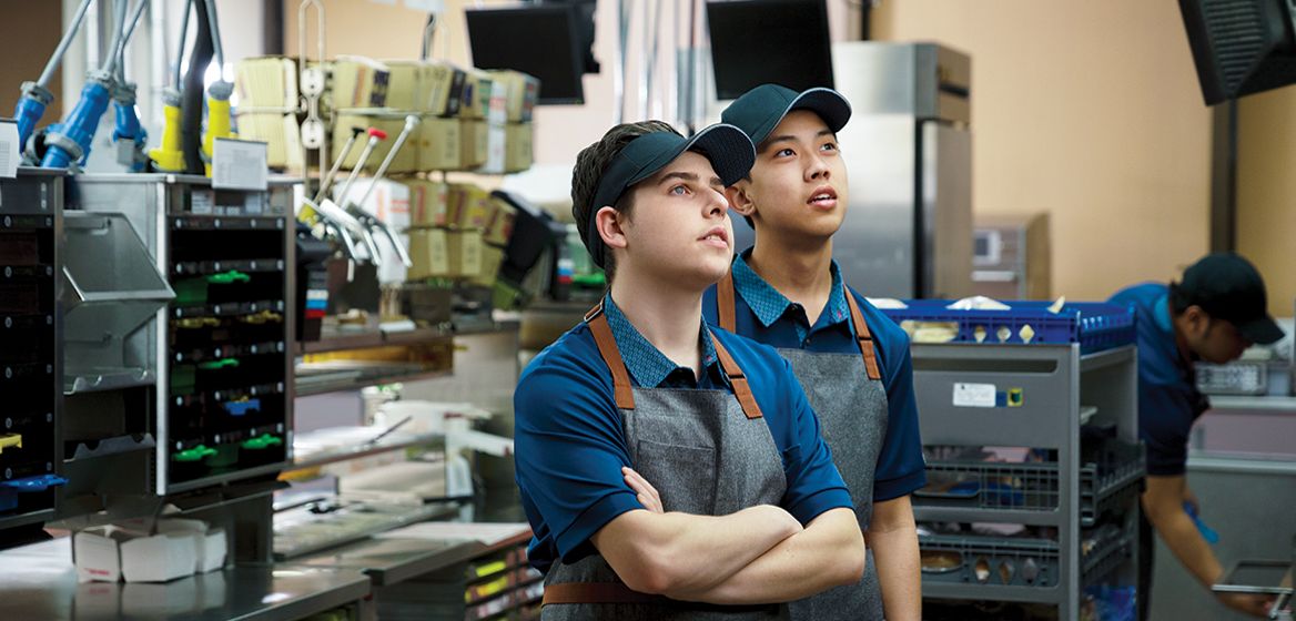 Two McDonald's staff member reading an incoming order on a tv monitor