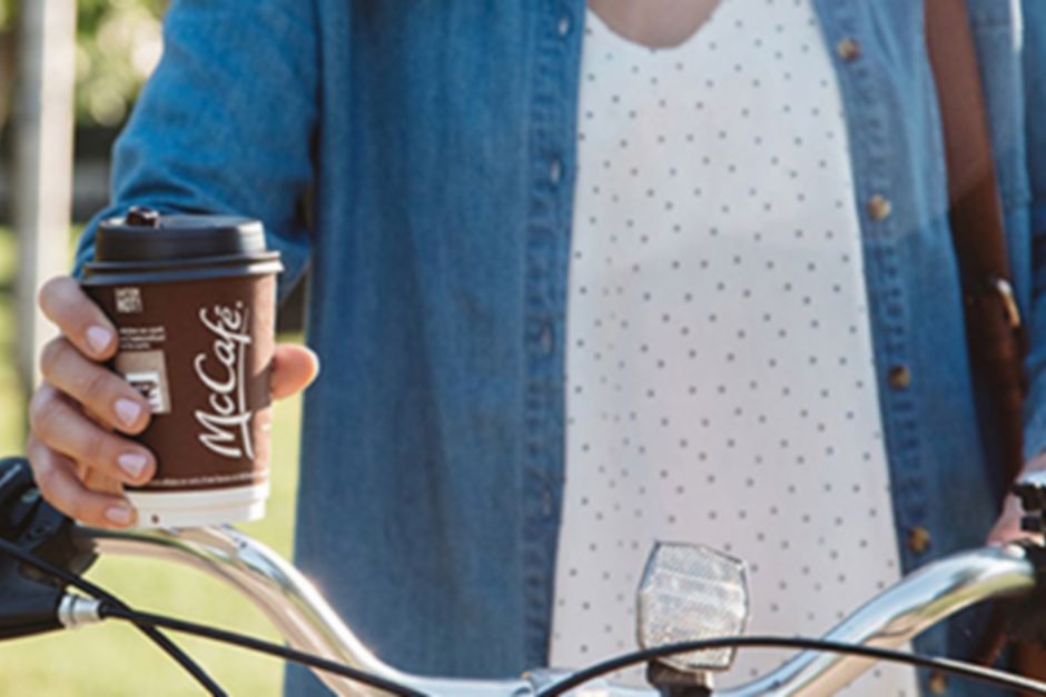 Une femme qui marche avec son vélo, un verre de café McCafé à la main
