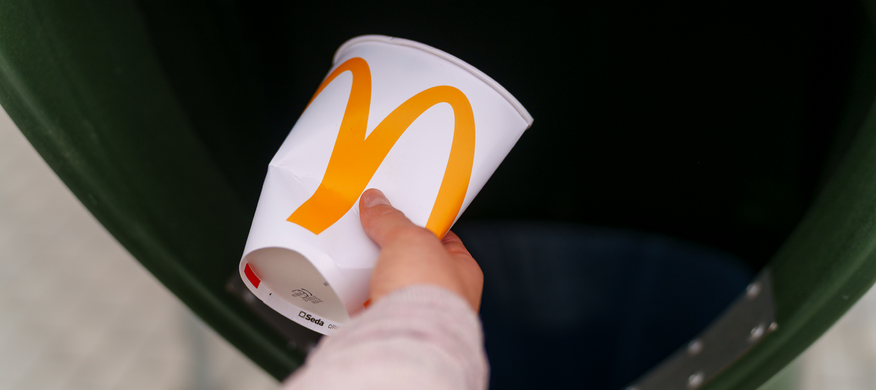 Hand wirft einen McDonald's Getränkebecher in einen Abfalleimer