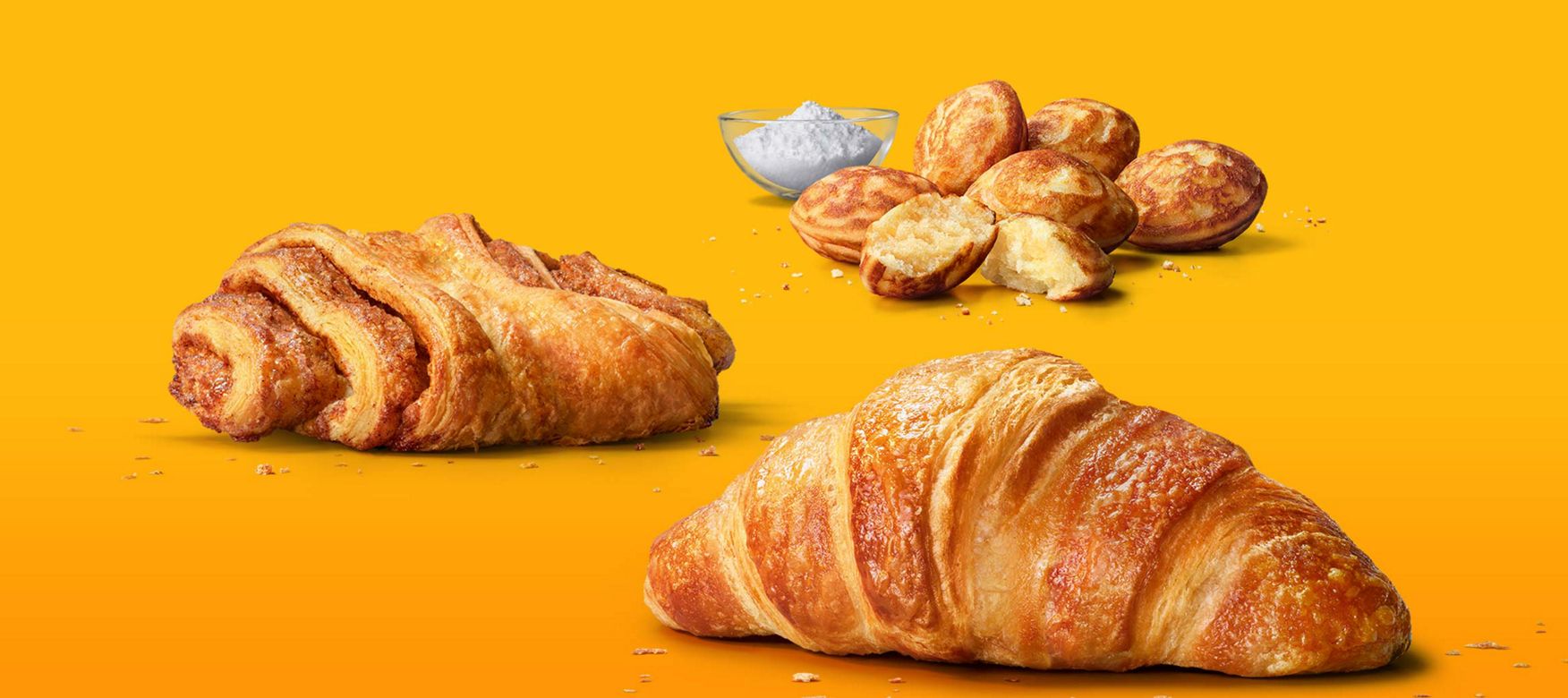 Das Bild zeigt ein Franzbrötchen, ein Buttercroissant und Mini Pancakes mit Puderzucker.