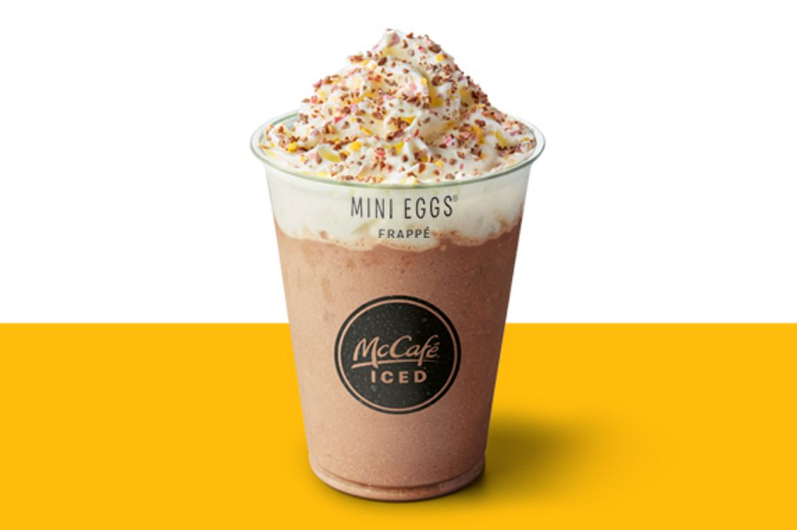 Iced McCafé Cadbury Mini Eggs frappe topped with whipped cream and sprinkles, shown on a yellow and white background.