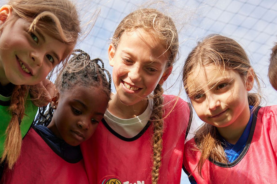 Children standing in a circle looking down during a Fun Football session.