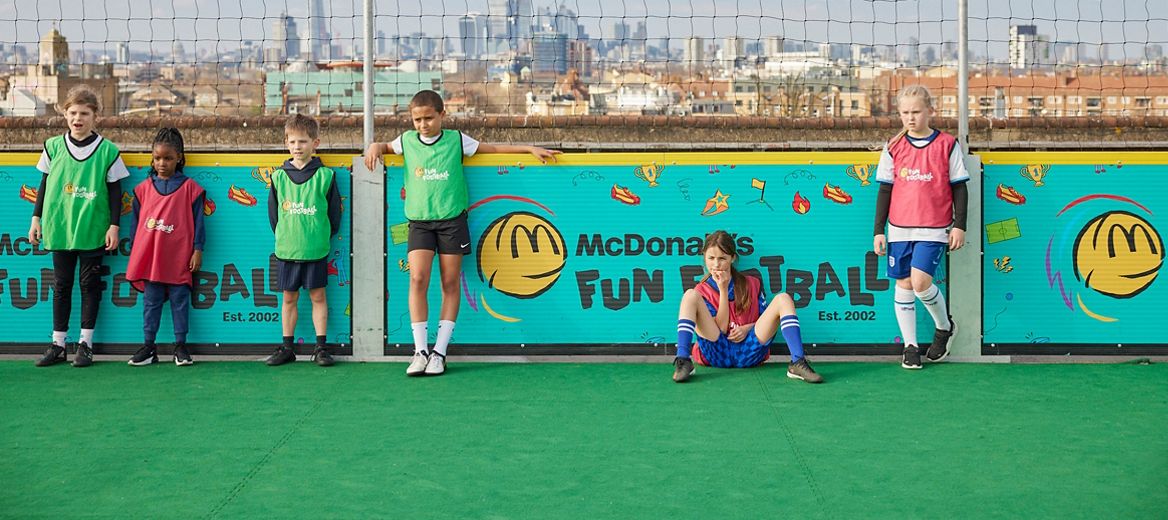 Children wearing Fun Football bibs gathered together on an outdoor football pitch.