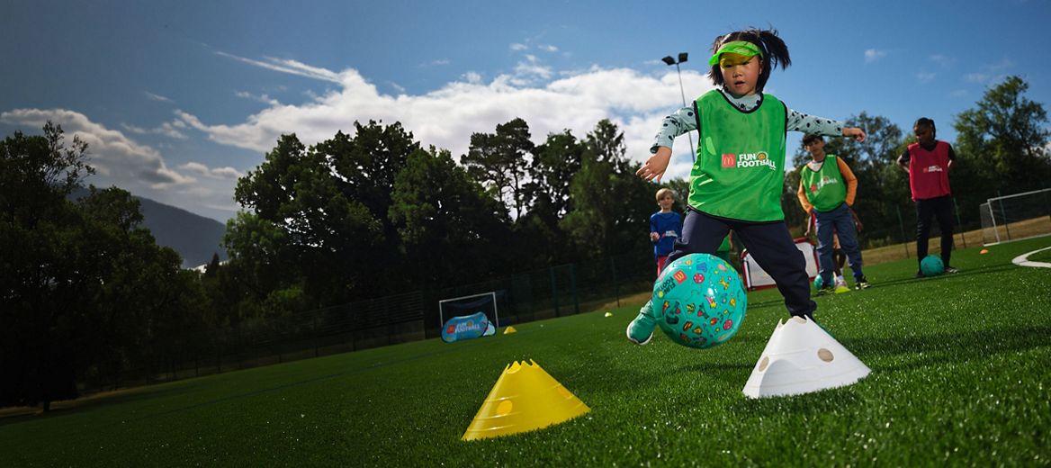 Child playing with a blue fun football on a grass pitch with cones.