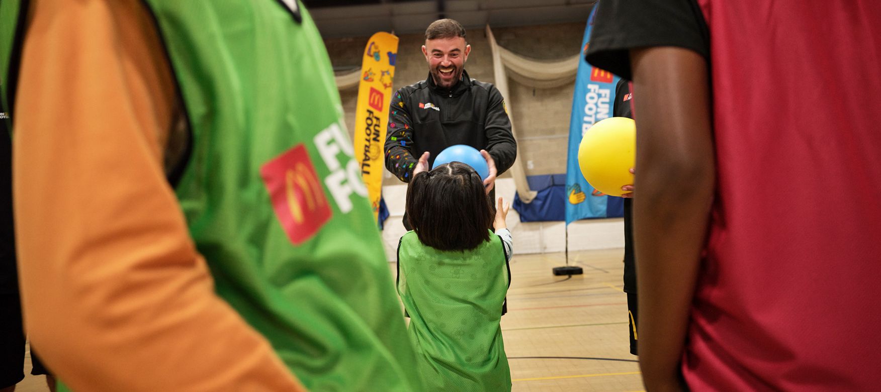 Coach holding a blue fun football with the silhouette of other children around.