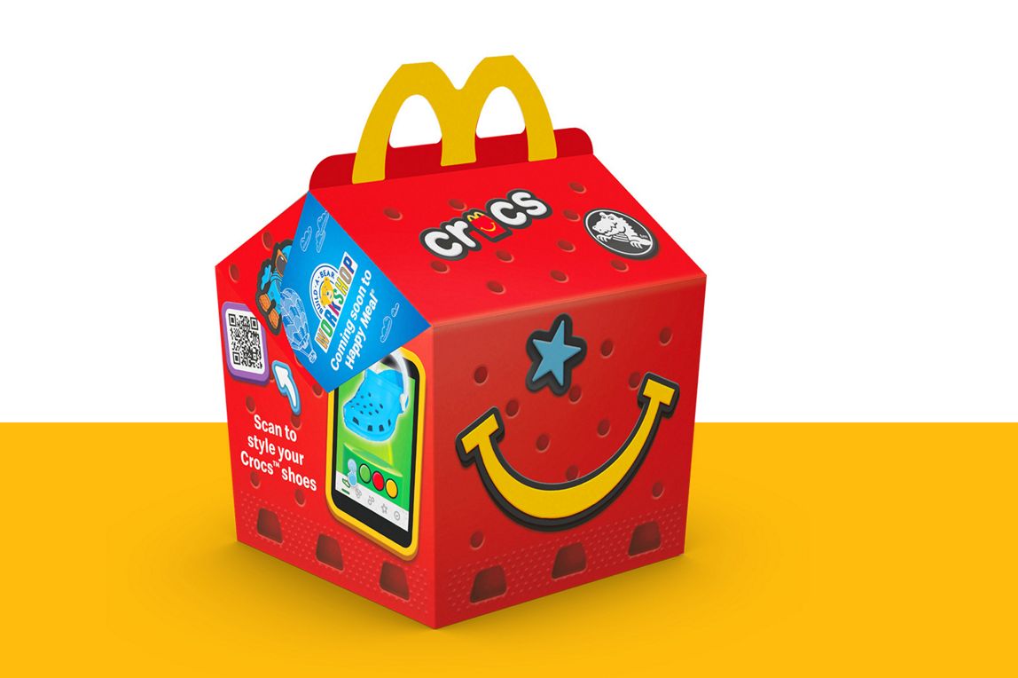 Crocs-themed Happy Meal box displayed on a yellow surface.