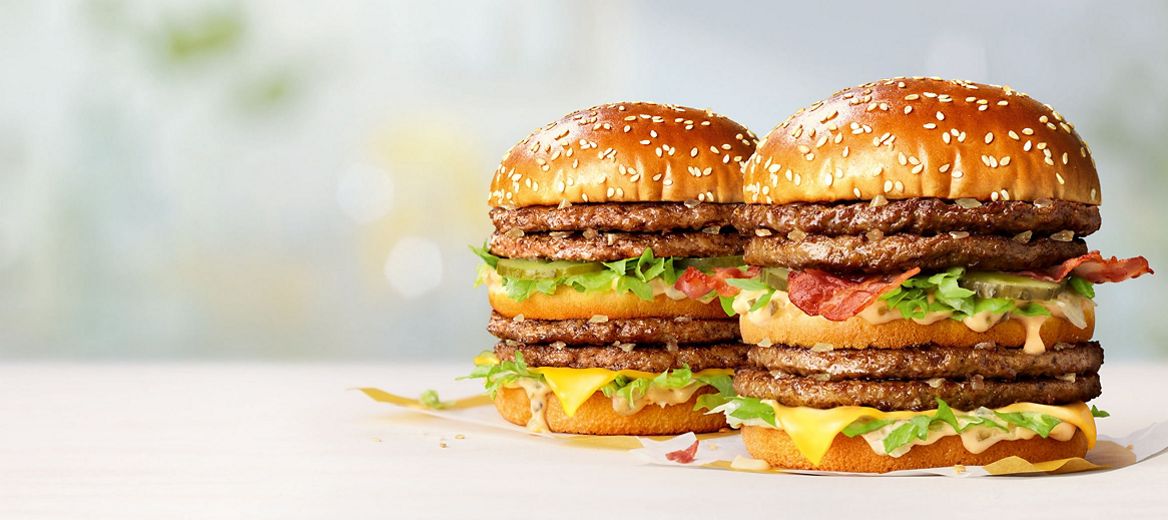 wo Double Big Mac burgers side by side on a light surface, with sesame buns, layered beef patties, lettuce, cheese, and sauce.