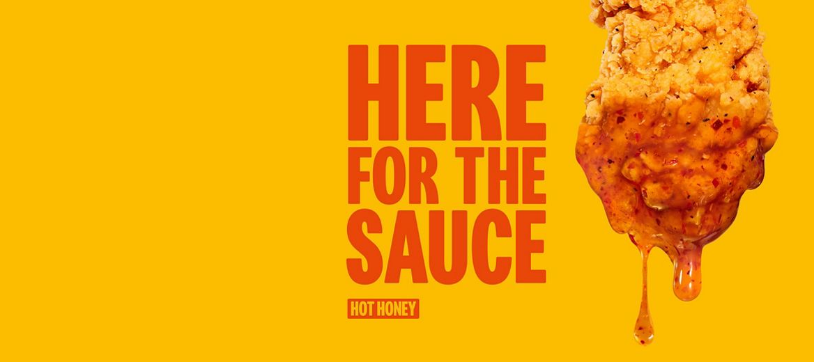 Crispy chicken dipped in Hot Honey sauce beside the words “Here for the Sauce” on a yellow background.