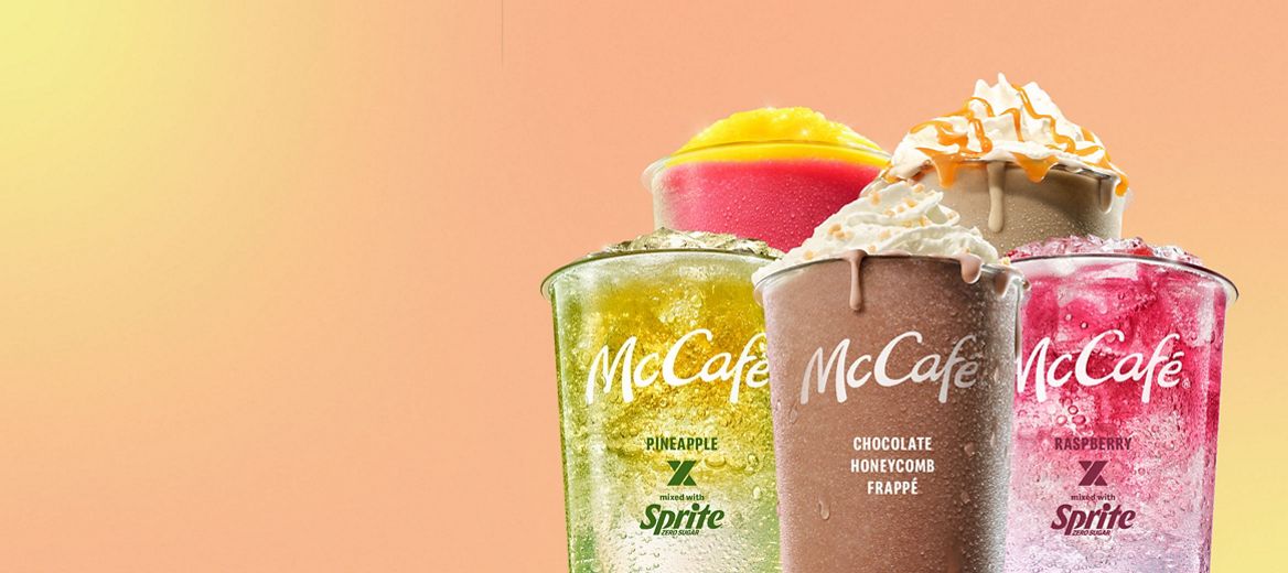 A selection of McCafé cold drinks including a Chocolate Honeycomb Frappe, Pineapple x Sprite Mixology, Raspberry x Sprite Mixology, Strawberry Lemonade and Caramel Frappe against a peach and yellow background.
