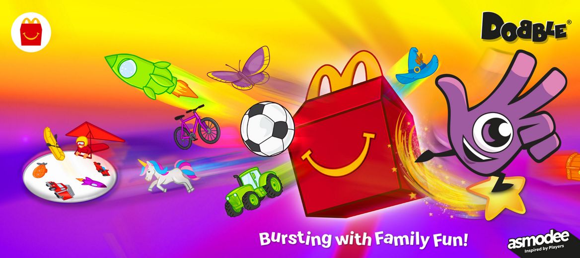 A bright, colourful scene with the Dobbly and a Happy Meal box surrounded by flying illustrated objects like rockets, animals, bikes and treasure chests.