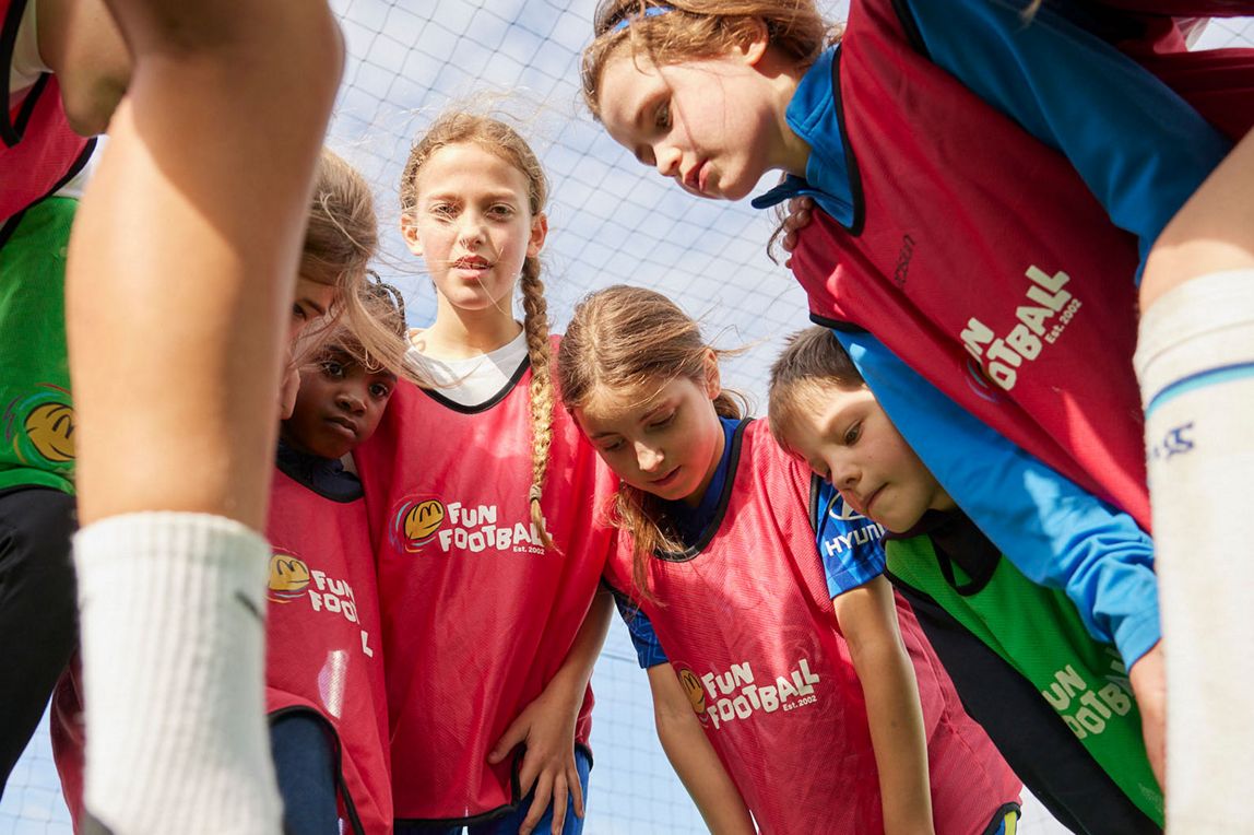 Children standing in a circle looking down during a Fun Football session.