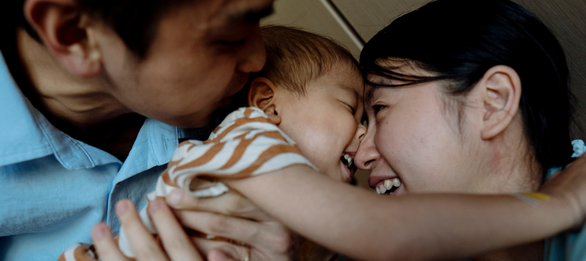 An image of two parents smiling and kissing their young child. 