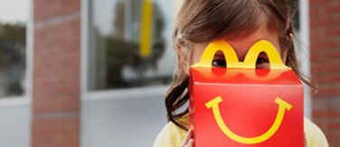 Young girl looking through Happy Meal box handles.