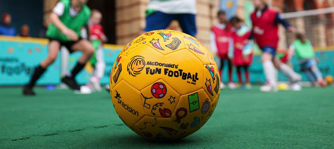 Close-up of a Fun Football football on a pitch with children playing behind it.