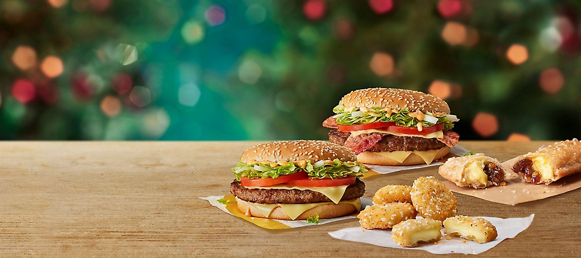  Big Tasty, Big Tasty with Bacon, Cheese Melt Dippers and a Festive Pie on a table with a Christmas background.