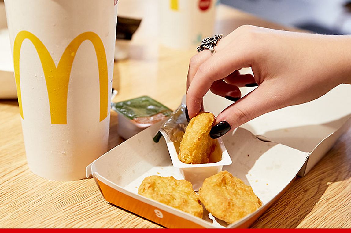 A hand is grabbing some chicken nuggets and dipping in a sauce packet.