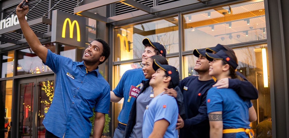 Seven McDonald's employees standing together outside a restaurant taking a photo