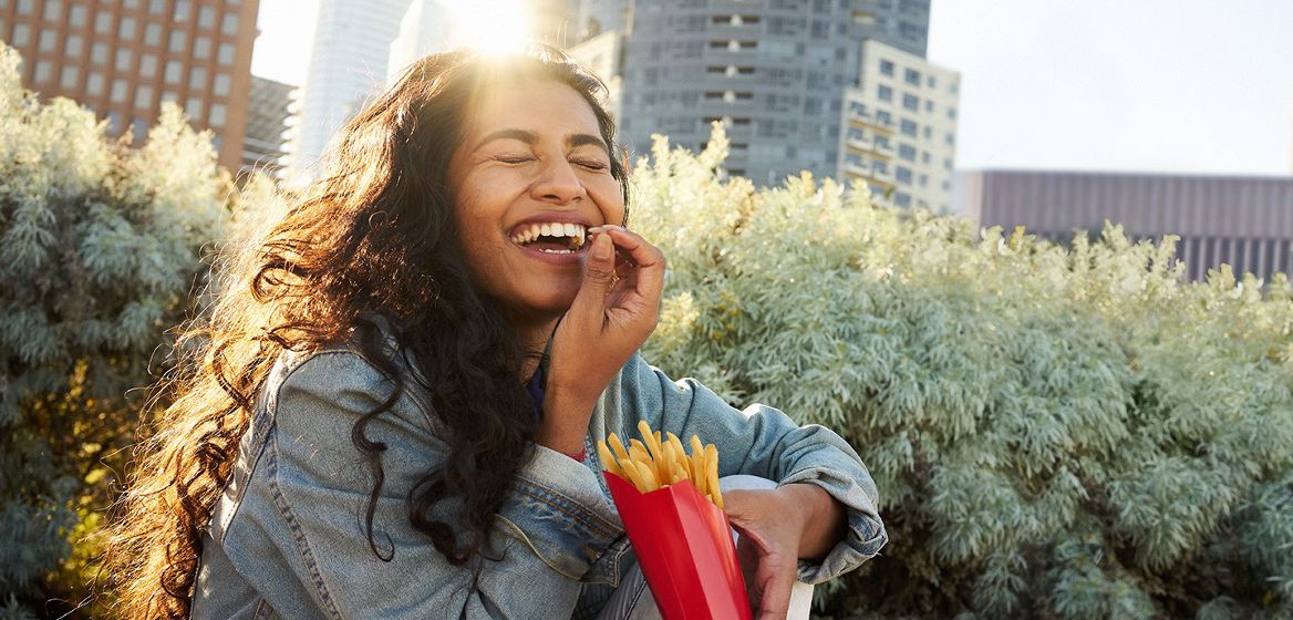 A woman smiling in the sun holding fries