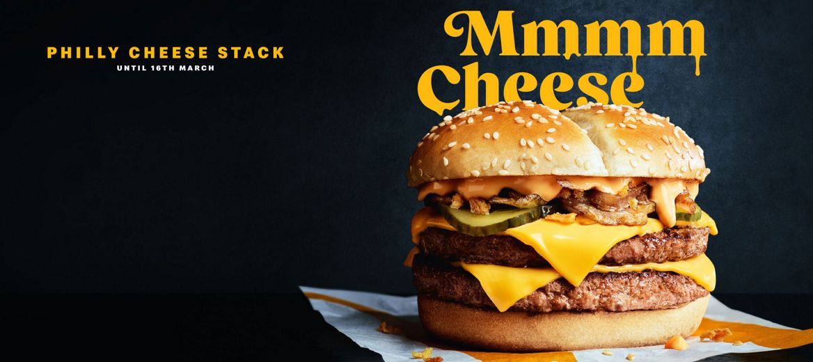 A double beef burger stacked with melted cheese, onions, pickles and sauce in a sesame bun, with the words “Philly Cheese Stack” displayed beside it.