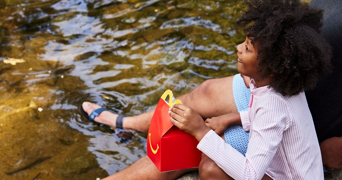 child with happy meal, smiling by water