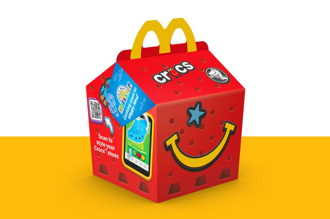 Crocs-themed Happy Meal box displayed on a yellow surface.