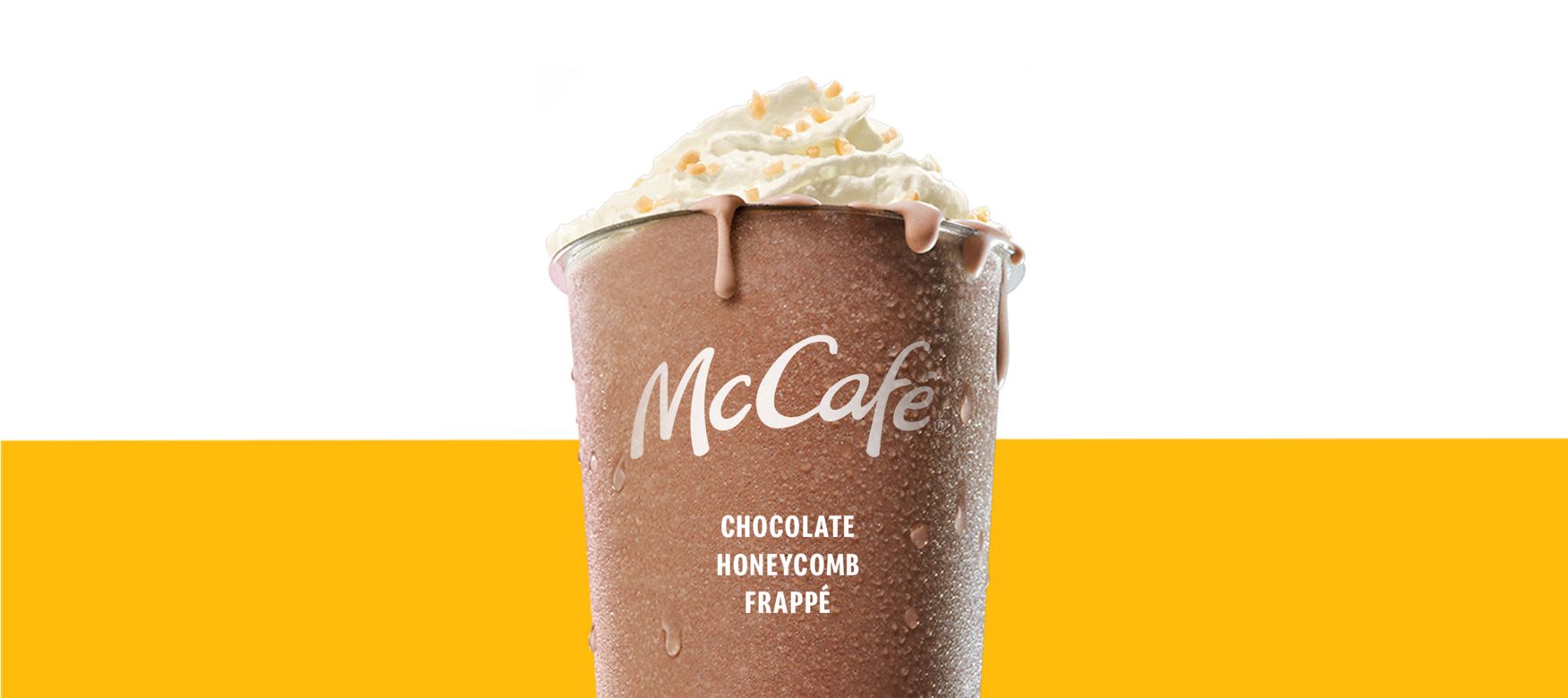 Chocolate Honeycomb Frappe in a chilled McCafé cup, topped with whipped cream and chocolate drizzle against a soft pink and yellow background.