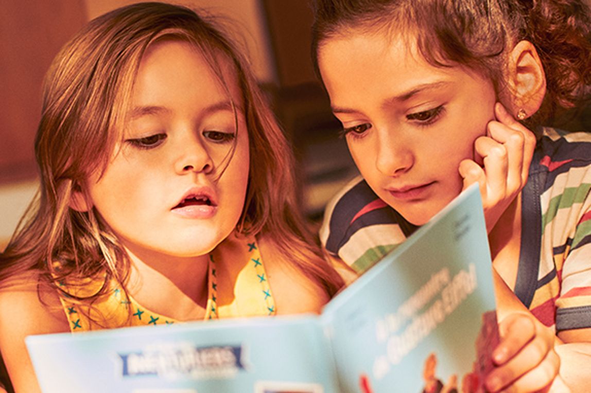 Two young girls reading book together, with red Happy Meal box beside them