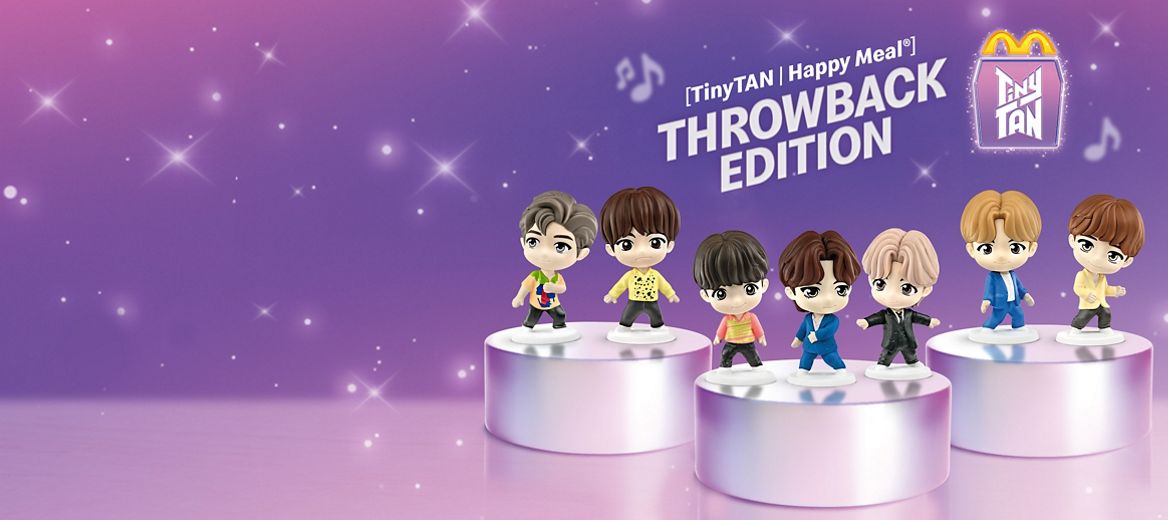 A static image that shows two toy collections. In the back, the Throwback edition has the seven TinyTAN characters on two podiums in their iconic outfits. In front, the Encore edition shows the same seven characters across two podiums, wearing themed merchandise. On the left, a white McDonald’s Happy Meal box reads ‘TinyTAN’ in large purple letters, with light rays and musical notes behind it.