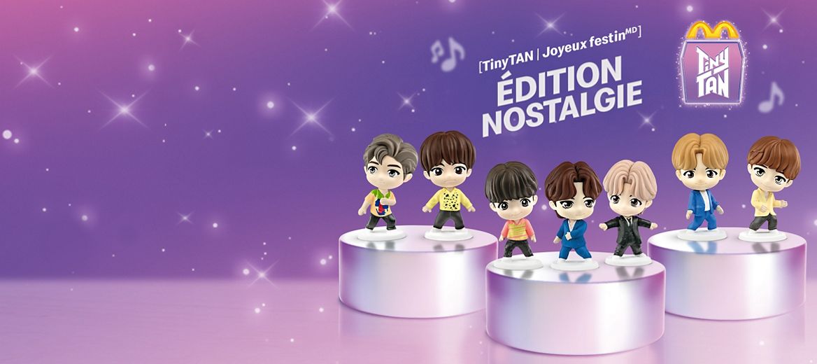 Une image fixe qui montre deux collections de jouets. À l’arrière, l’édition « Throwback » présente les sept personnages TinyTAN sur deux podiums, avec leurs tenues emblématiques. À l’avant, l’édition « Encore » montre les sept mêmes personnages sur deux podiums, portant des articles thématiques. À gauche, une boîte Joyeux festin de McDonald’s blanche affiche « TinyTAN » en grosses lettres mauves, avec des rayons de lumière et des notes de musique derrière.