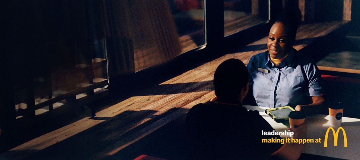 Two McDonald’s crew members sit across from each other at a table inside the restaurant.