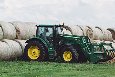 Un tracteur vert devant plusieurs balles de foin par une belle journée ensoleillée