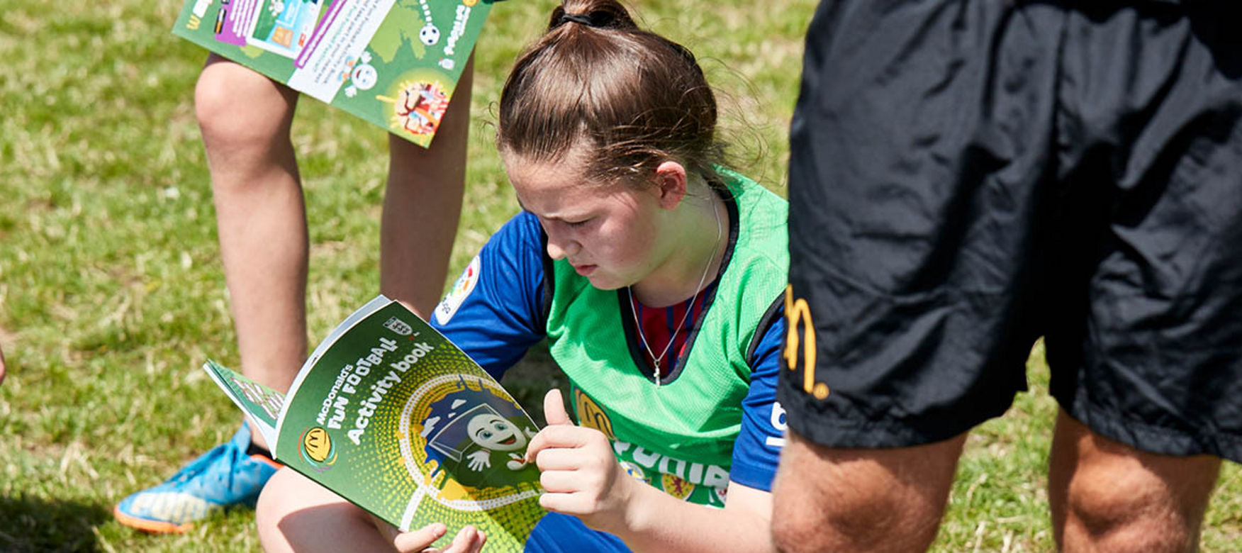 Two girls and coach at a McDonald’s Fun Football session reading the fun Football activity book