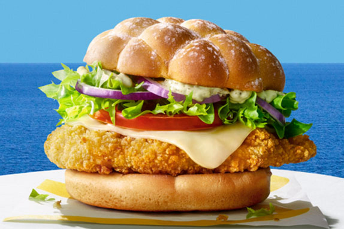 A delicious looking Chicken burger on a white tablecloth in front of a seascape background.