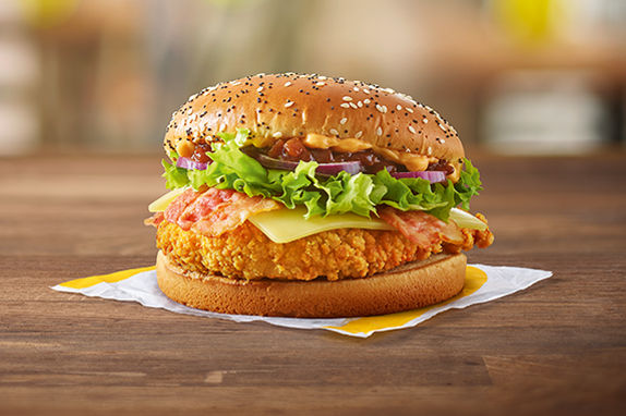 Picture of a crispy chicken burger with lettuce, onion, cheese between a seeded bun. 