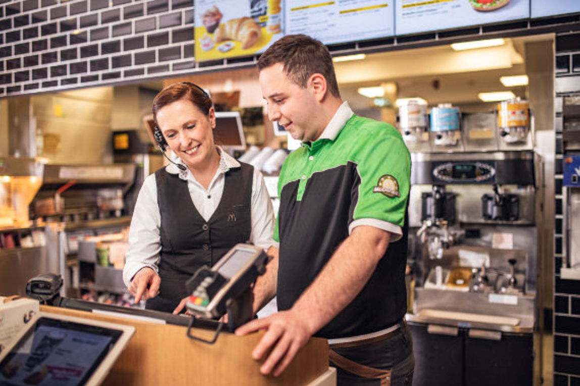 Eine Restaurant Managerin zeigt einem McDonald's Mitarbeiter das Kassensystem