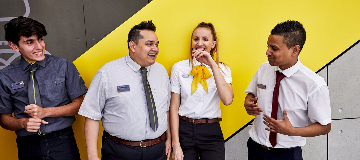Four McDonald's employees standing together outside of a restaurant smiling and laughing