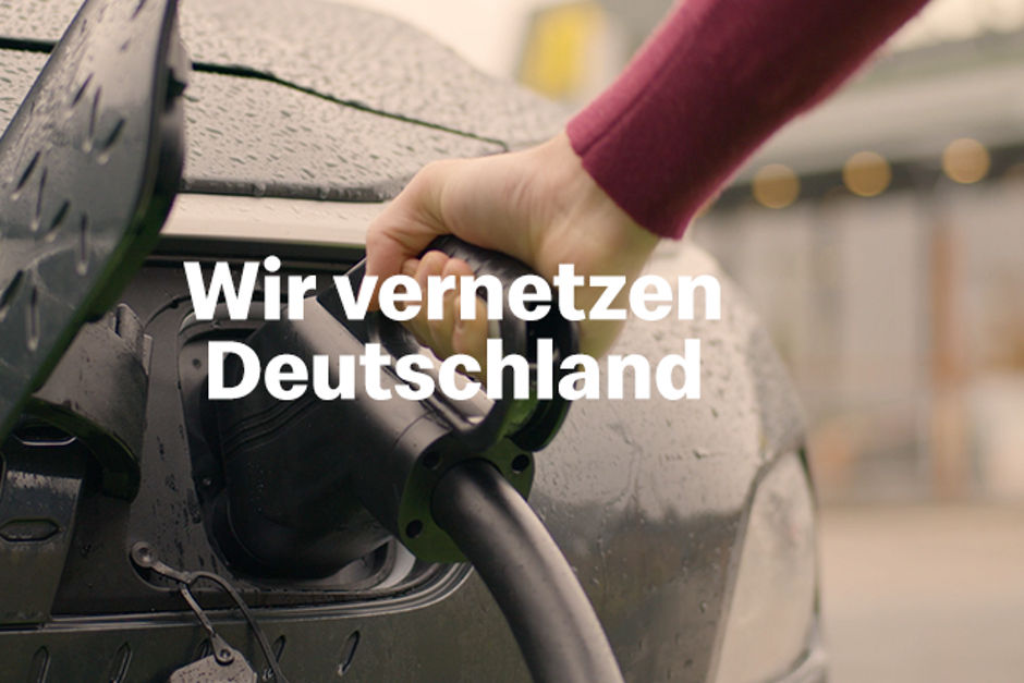 Ladestecker in die Ladebuchse eines E-Autos. Text: Wir vernetzen Deutschland.