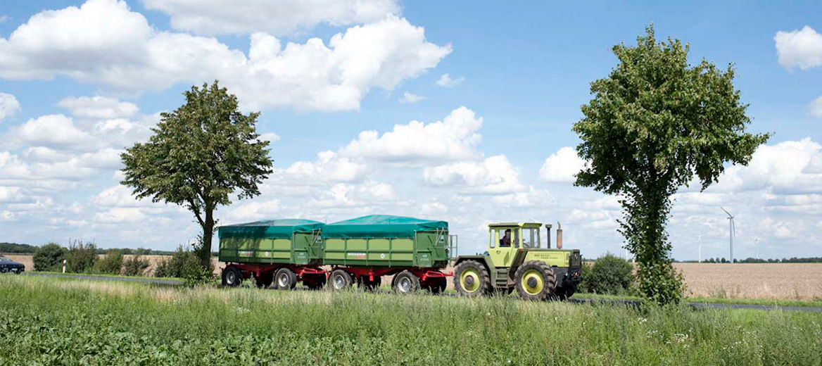 Traktor mit zwei Anhängern fährt eine Landstraße entlang